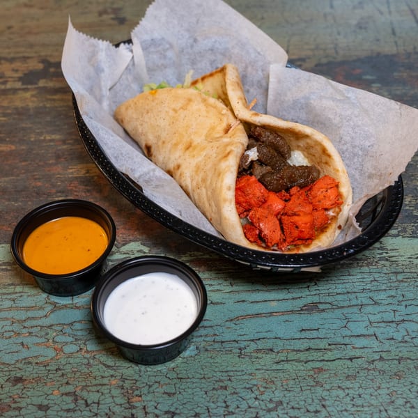 DC BITES halal chicken and beef shawarma in pita with two dipping sauces on a distressed wooden table.
