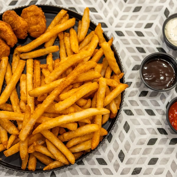 Crispy golden fries and fried bites fill a black platter, accompanied by creamy white, brown, and red dipping sauces.