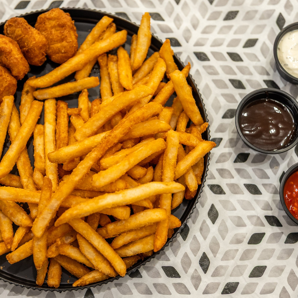 Crispy golden fries and fried bites fill a black platter, accompanied by creamy white, brown, and red dipping sauces.