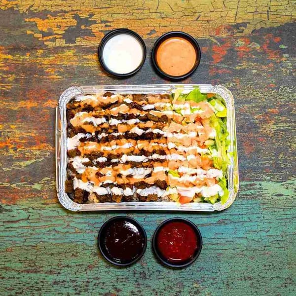 DC BITES halal platter with meat, rice, and salad, drizzled with white and orange sauces, with four side sauces.