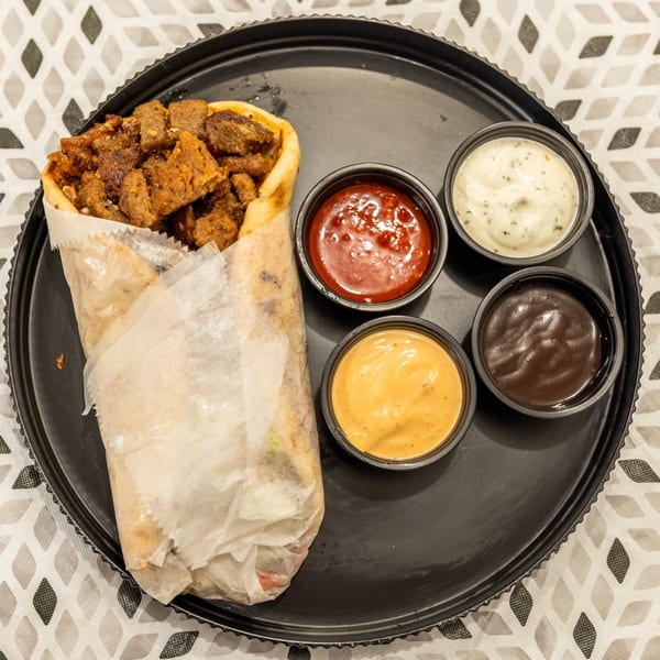 Loaded pita wrap with seasoned meat and four dipping sauces on a black serving tray.