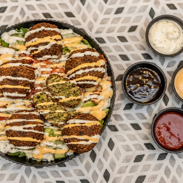 Platter of falafel sandwiches with lettuce and sauces, accompanied by bowls of white, brown, orange, and red dipping sauces.
