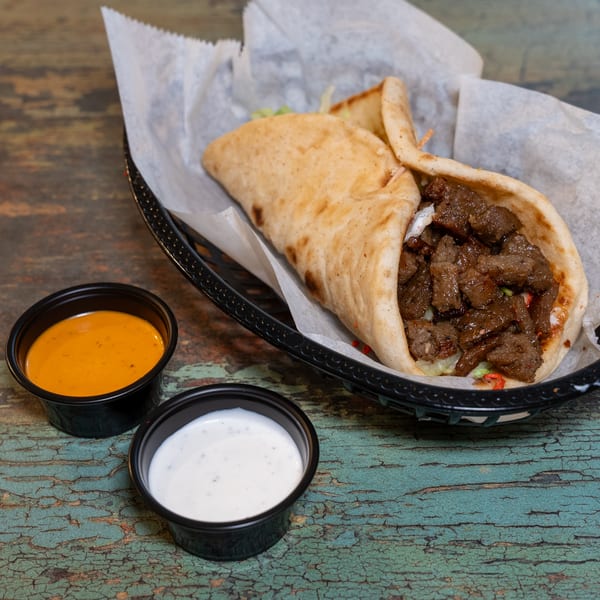 DC BITES halal beef shawarma in pita bread with white and orange sauces on a rustic table.