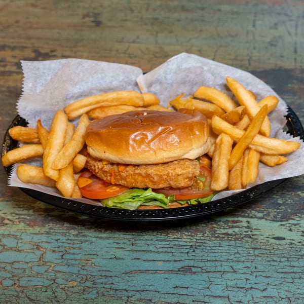 A crispy chicken sandwich with lettuce, tomato, and sauce, served with a side of golden fries.