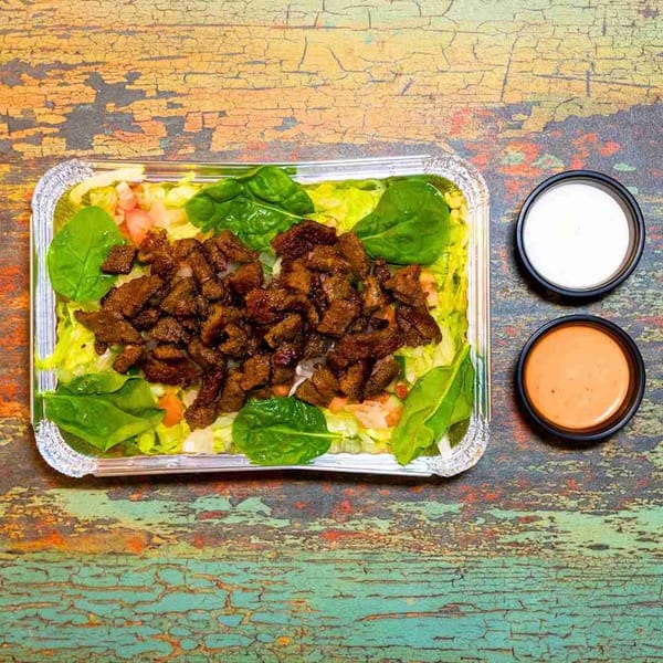 DC BITES halal platter with meat, lettuce, spinach, tomatoes, and two sauces on a rustic table.