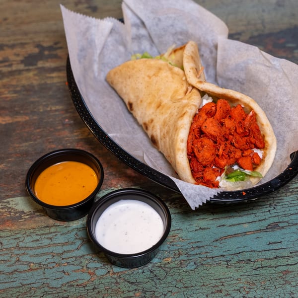 Halal chicken gyro with red sauce and white sauce on a rustic wooden table.