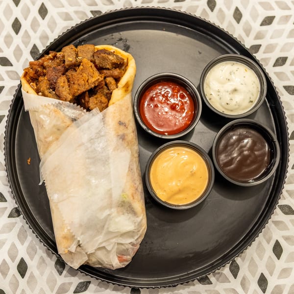 Loaded gyro wrap with seasoned meat and four dipping sauces on a black plate.