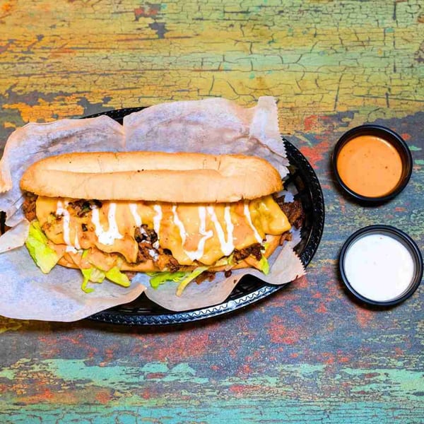 A DC BITES halal cheesesteak with lettuce, meat, cheese, and sauces, served with two dipping sauces.