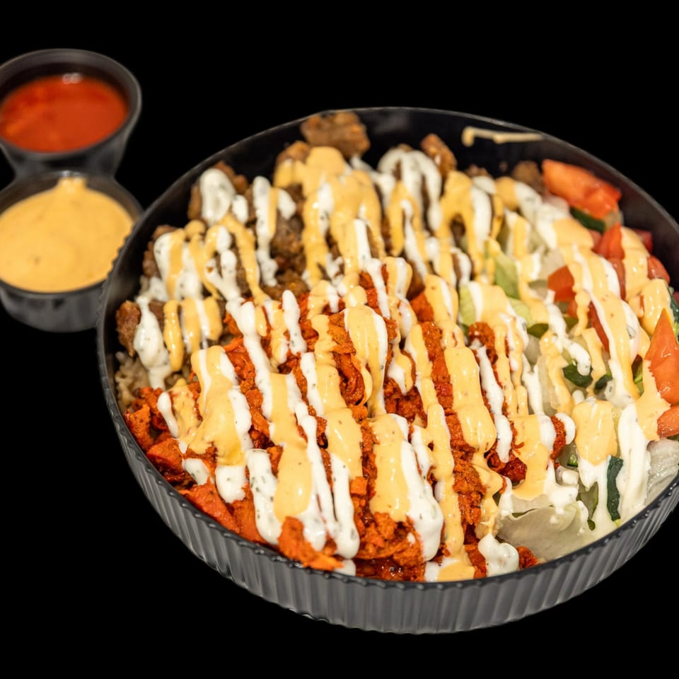 Loaded platter of seasoned fried chicken, vegetables, and rice drizzled with creamy orange and white sauces, served with dipping sauces.