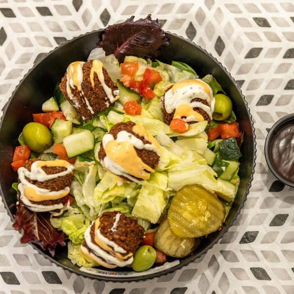 Salad bowl with falafel, lettuce, cucumbers, tomatoes, green olives, pickles, and drizzled creamy sauces.