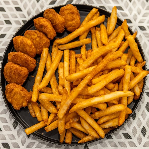 Black plate piled with golden French fries and several crispy breaded chicken nuggets on a patterned tablecloth.