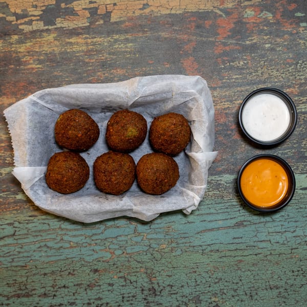 Six crispy falafel balls in a paper-lined tray with white and orange dipping sauces.